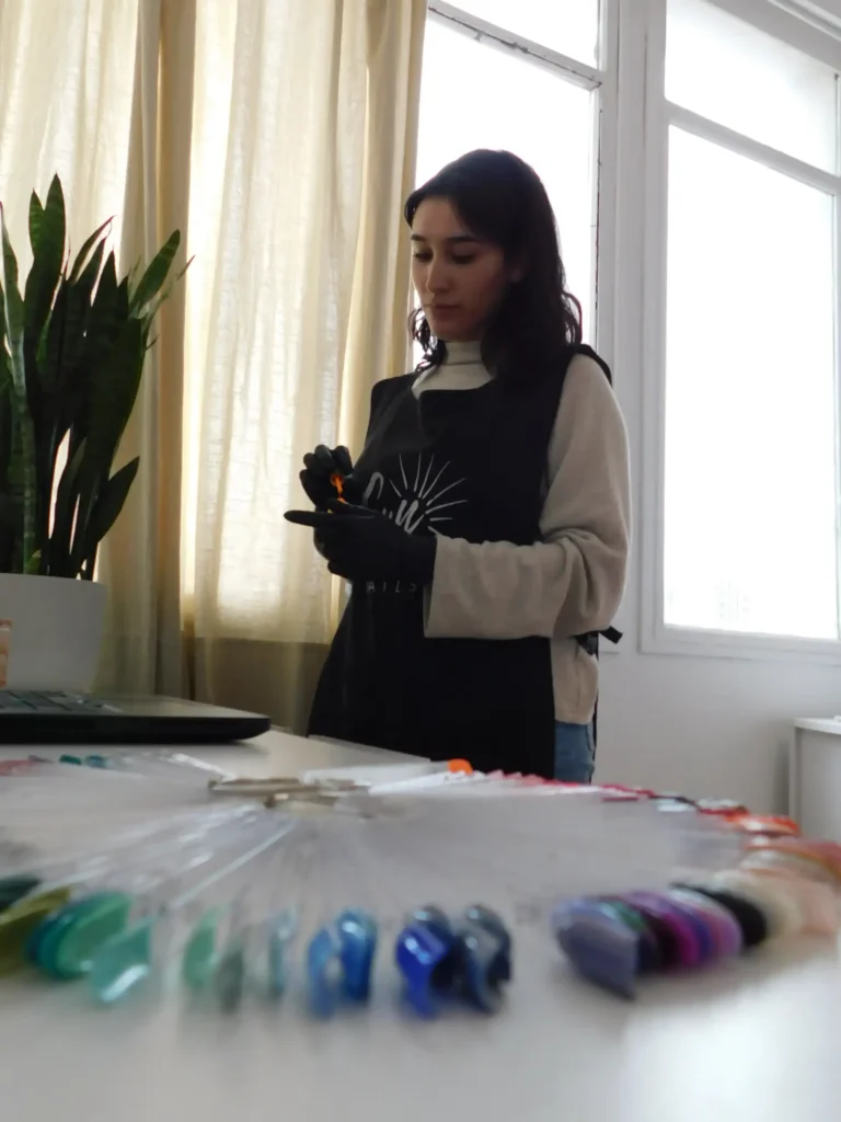 Manicurista en Sun Nails concentrada en su trabajo, con abanico de muestras de uñas y ambiente luminoso y profesional